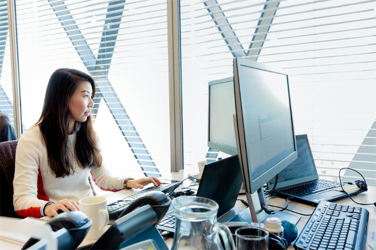 A person sitting at a desk using a laptop connected to desktop monitors.