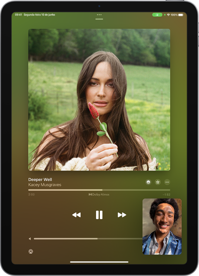 Uma ligação do FaceTime mostrando uma sessão do SharePlay com conteúdo de áudio do Apple Music sendo compartilhado em sincronia com todas as pessoas na ligação. Uma imagem da pessoa que está compartilhando o conteúdo aparece na parte inferior à direita, a imagem do álbum que está sendo compartilhado está na parte superior da tela, e os controles de reprodução estão abaixo da imagem do álbum.